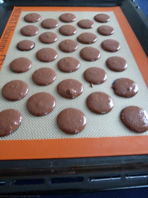 Die aufgespritzten Macaron-Tupfen auf einer Backmatte.